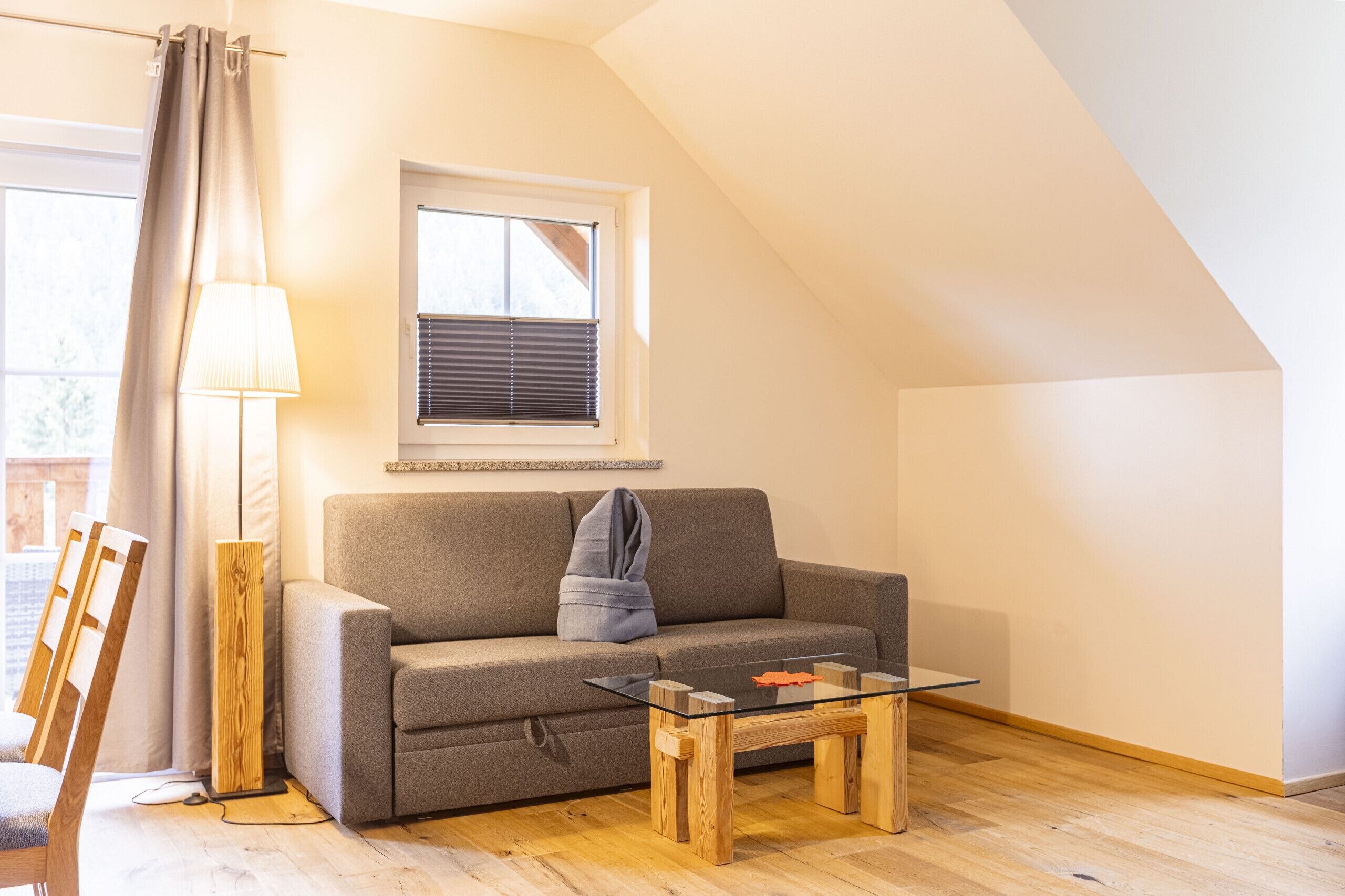 A cozy living room with a sofa, a glass coffee table, a lamp, and a window with blinds.