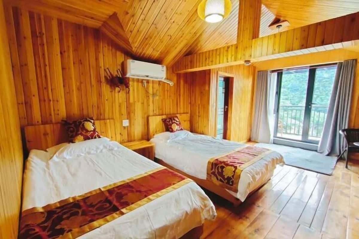 A wooden cabin room with two beds, a window, and an air conditioning unit.