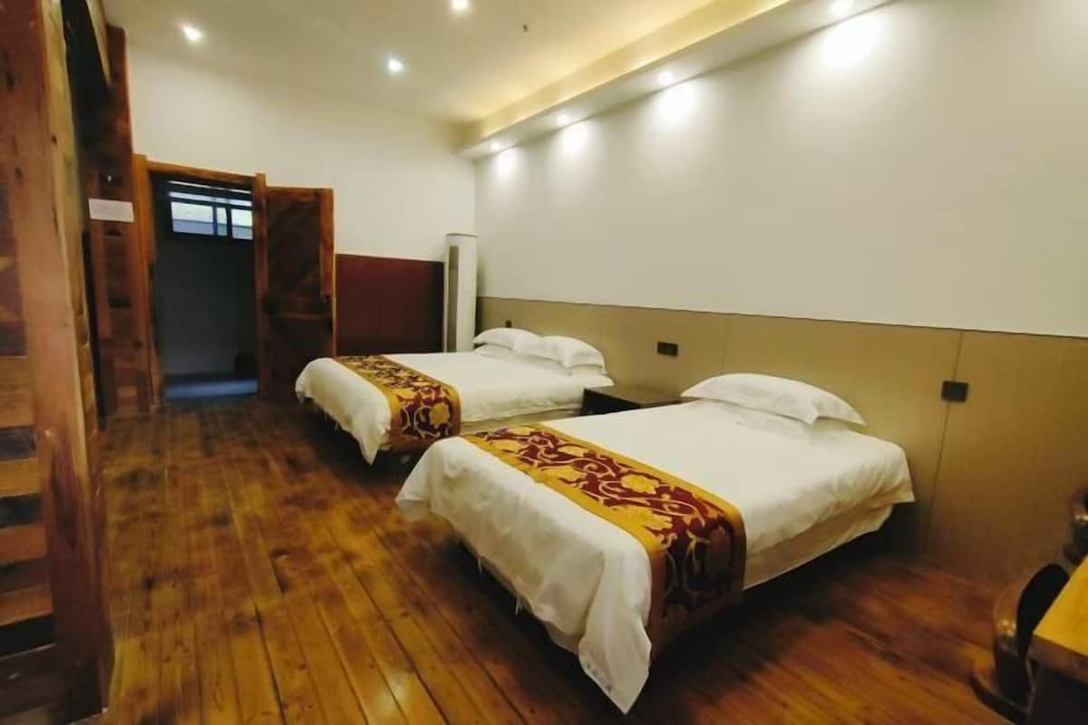 A hotel room with two beds, wooden flooring, and a door leading to a hallway.