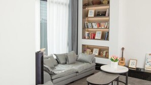 A modern living room with a grey sofa, a round coffee table, and a bookshelf filled with books and decorative items. - Xiyuan Villa (Deqing)