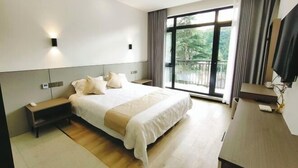 A modern hotel room with a large bed, bedside tables, a desk, and a balcony with a view of greenery. - Xiyuan Villa (Deqing)