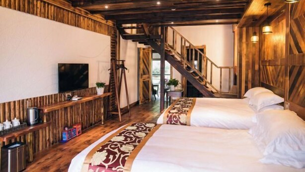 A room with wooden beams, a staircase, a bed with a patterned bedspread, a TV, and a small table with a kettle. - Xiyuan Villa (Deqing)