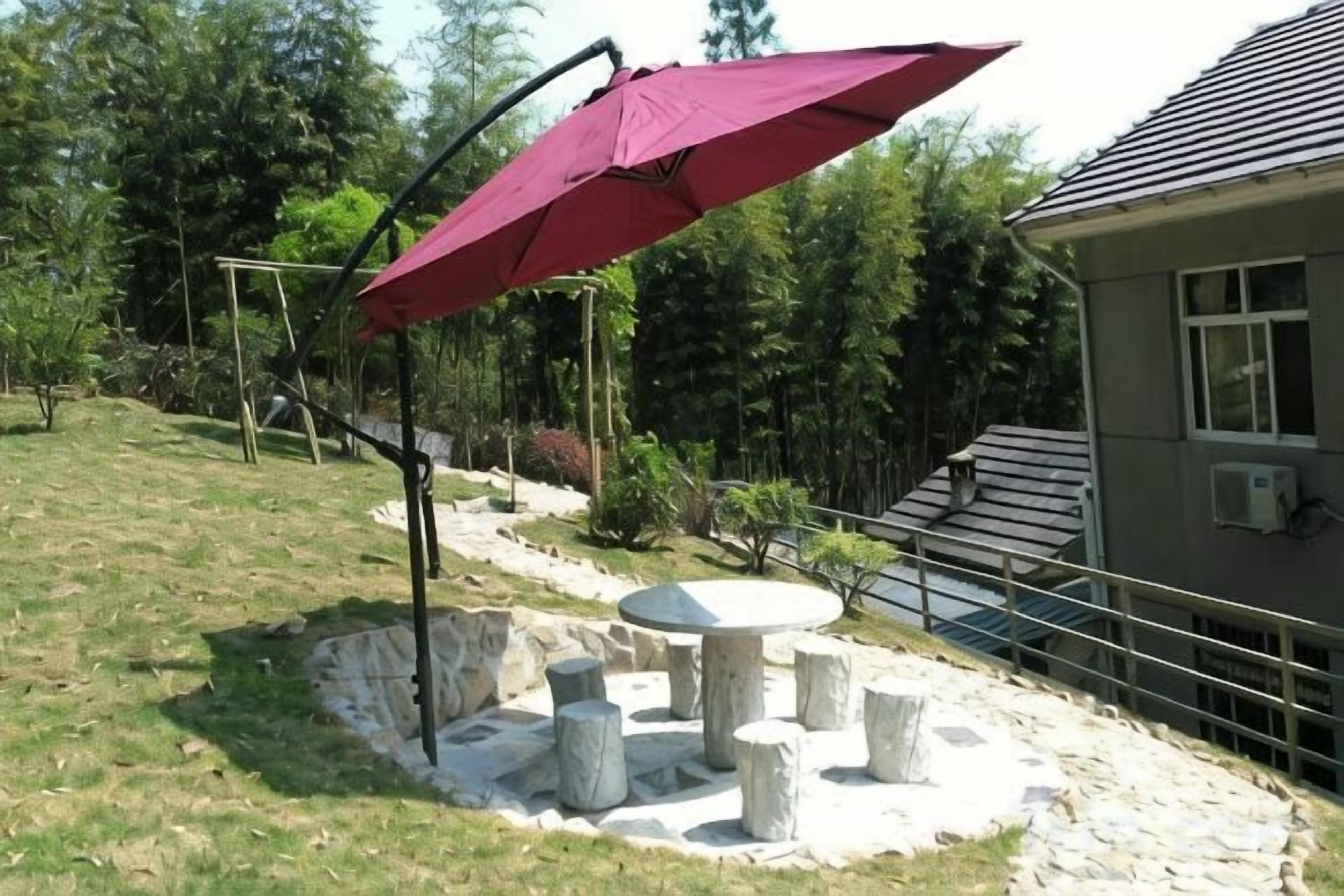 An outdoor seating area with a table and chairs, a pergola with a red umbrella, and a stone wall.