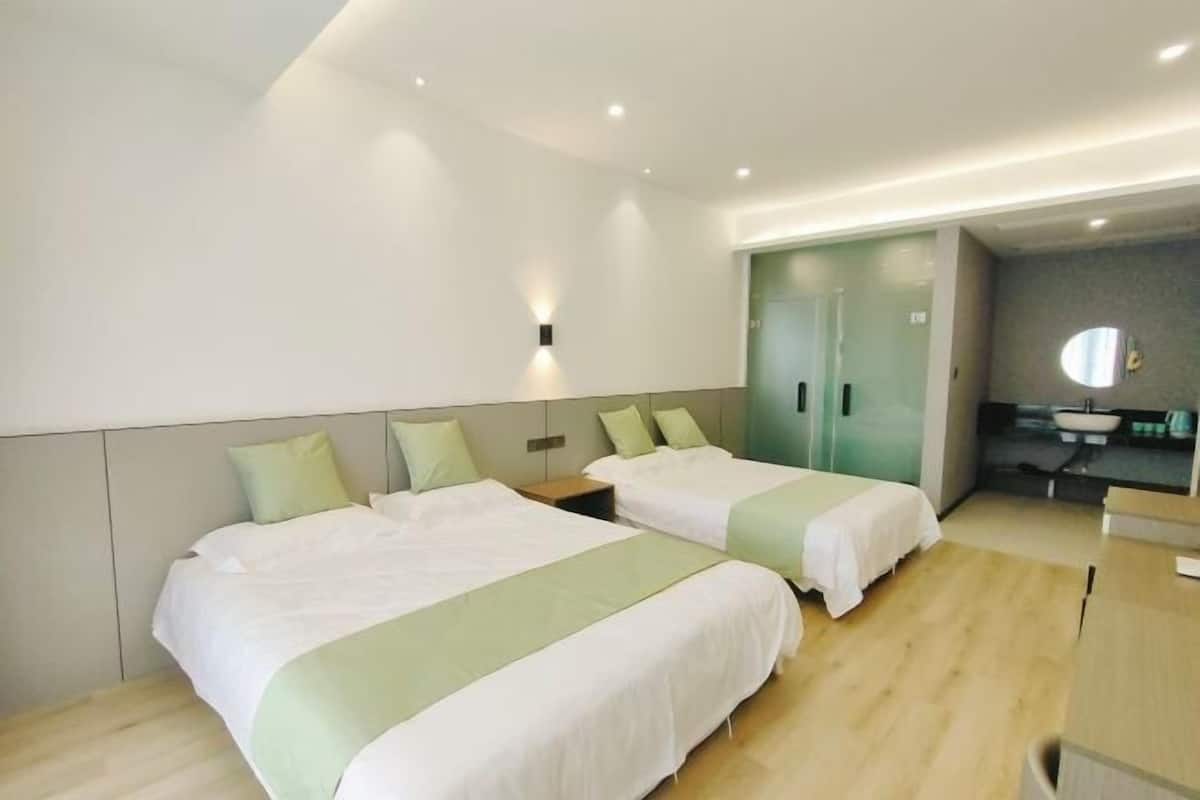 A hotel room with two beds, a small desk, a mirror, and a bathroom visible through a glass door.