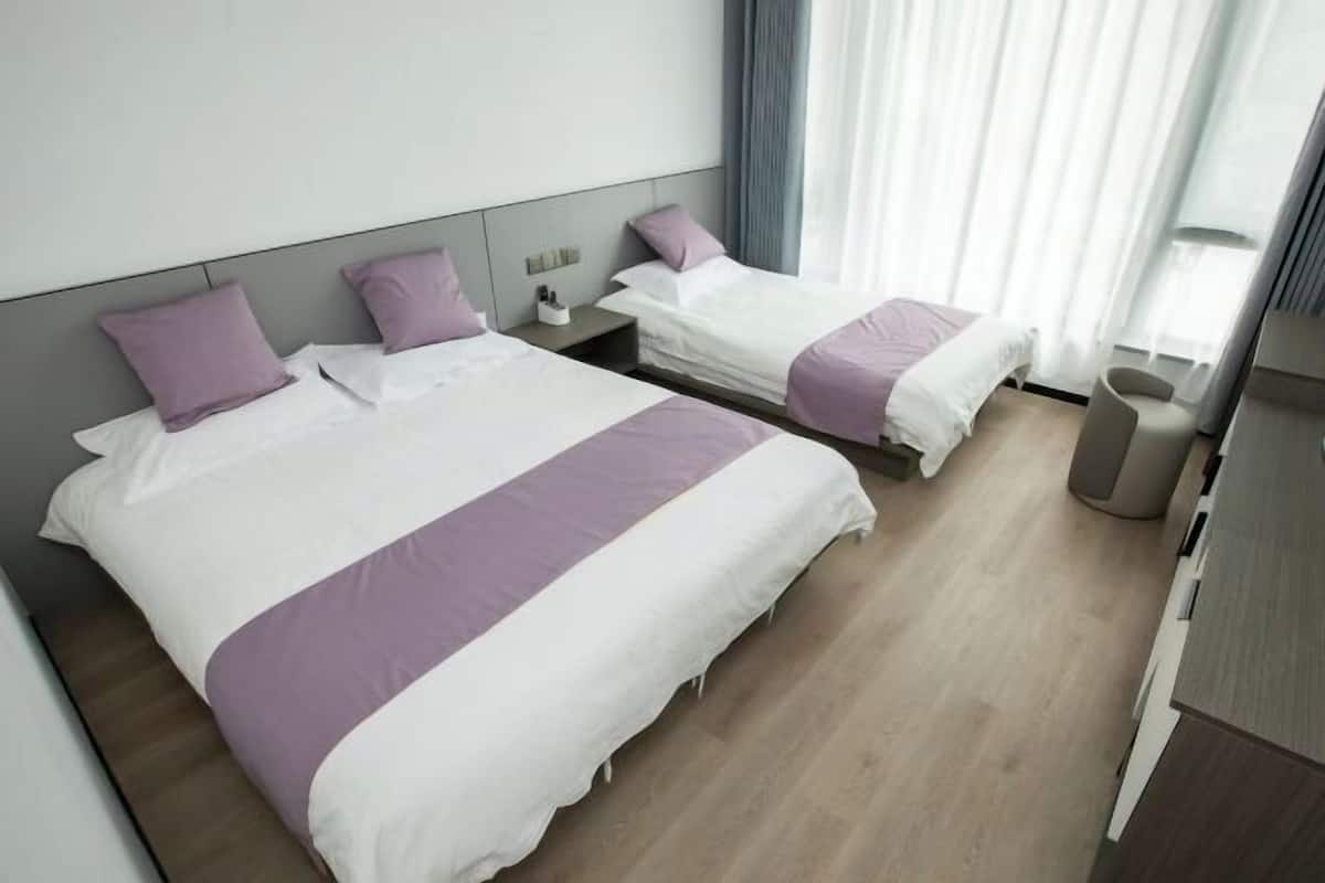 A hotel room with two beds, a bedside table, a chair, and a large window with curtains.
