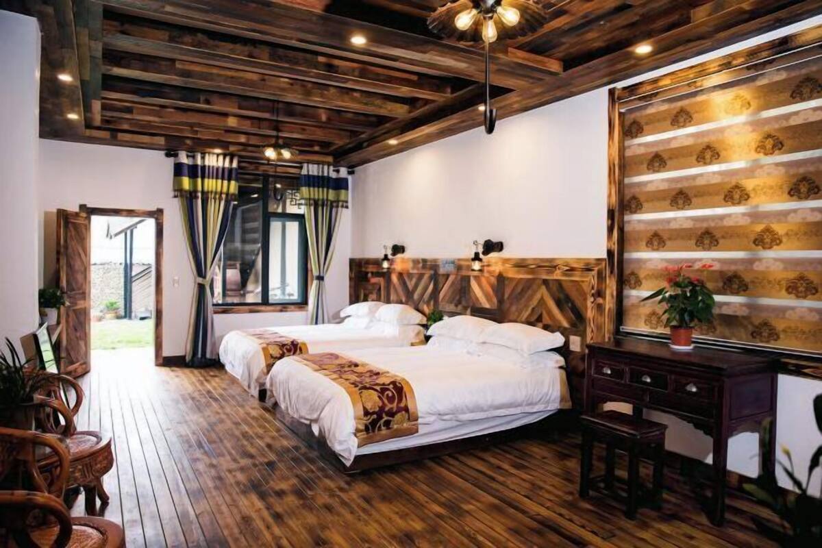 A room with wooden flooring, two beds, a desk, and a large window with curtains.