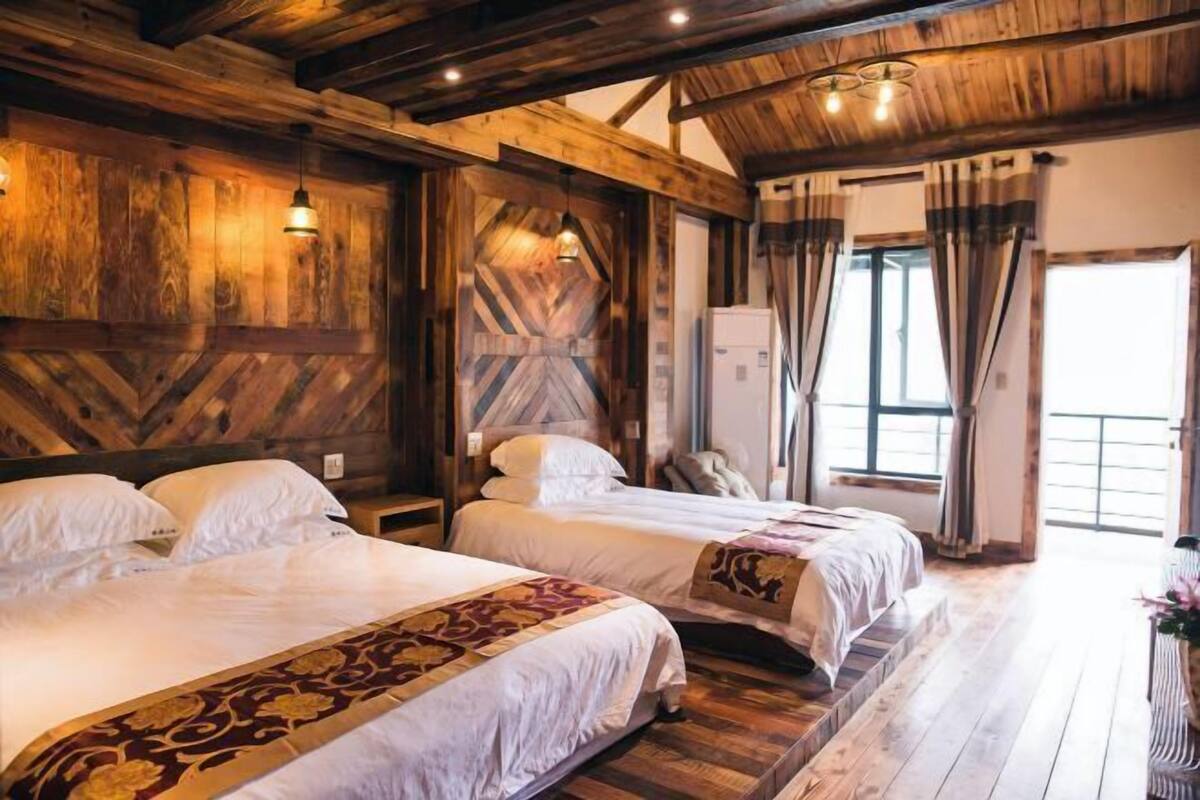 A room with two beds, wooden walls, a wooden ceiling, and a large window with curtains.