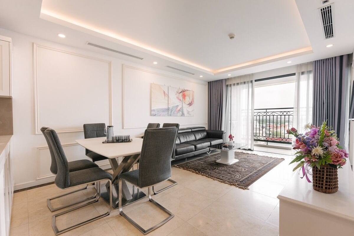 A modern living room with a dining area, a black leather sofa, a coffee table, and a large window with curtains.