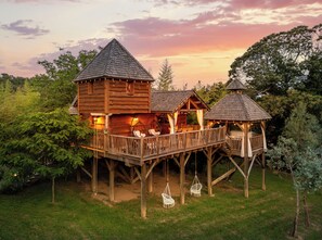 Eine Holzdiele mit einer Terrasse und zwei angebauten Gebäuden, umgeben von Bäumen.