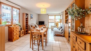 Un salon chaleureux avec une table à manger en bois, un canapé et un téléviseur. On y trouve également des meubles de rangement en bois et une bibliothèque.