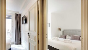 A hotel room with a bed, a television mounted on the wall, and a view of the outside balcony. - Résidence Paris CHARONNE (Paris)
