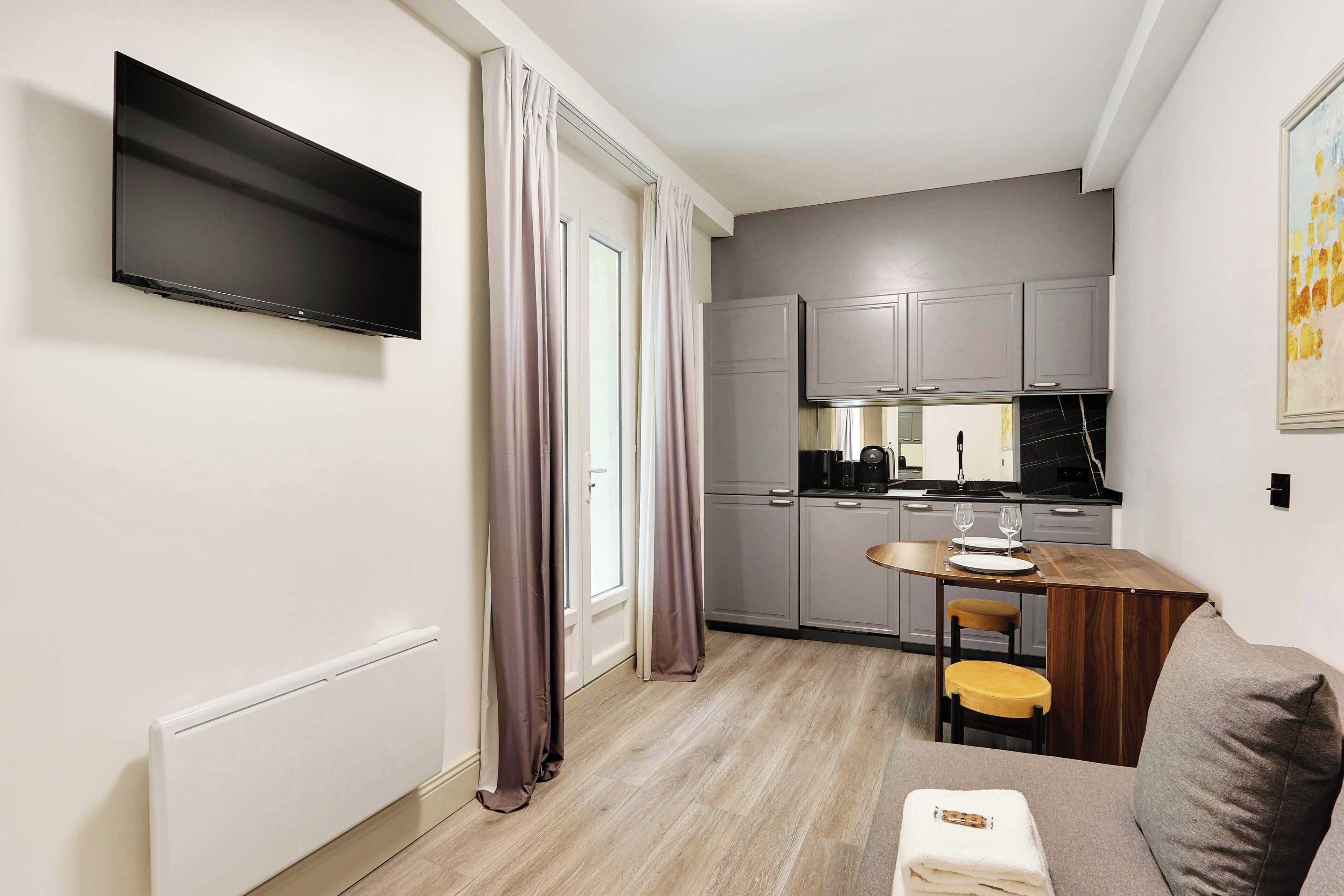 Una cocina moderna con gabinetes grises, una encimera negra y un comedor con una mesa de madera y dos sillas.