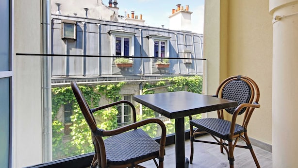 A balcony with a table and two wicker chairs, overlooking a building with windows and a view of greenery. - Résidence Paris CHARONNE (Paris)