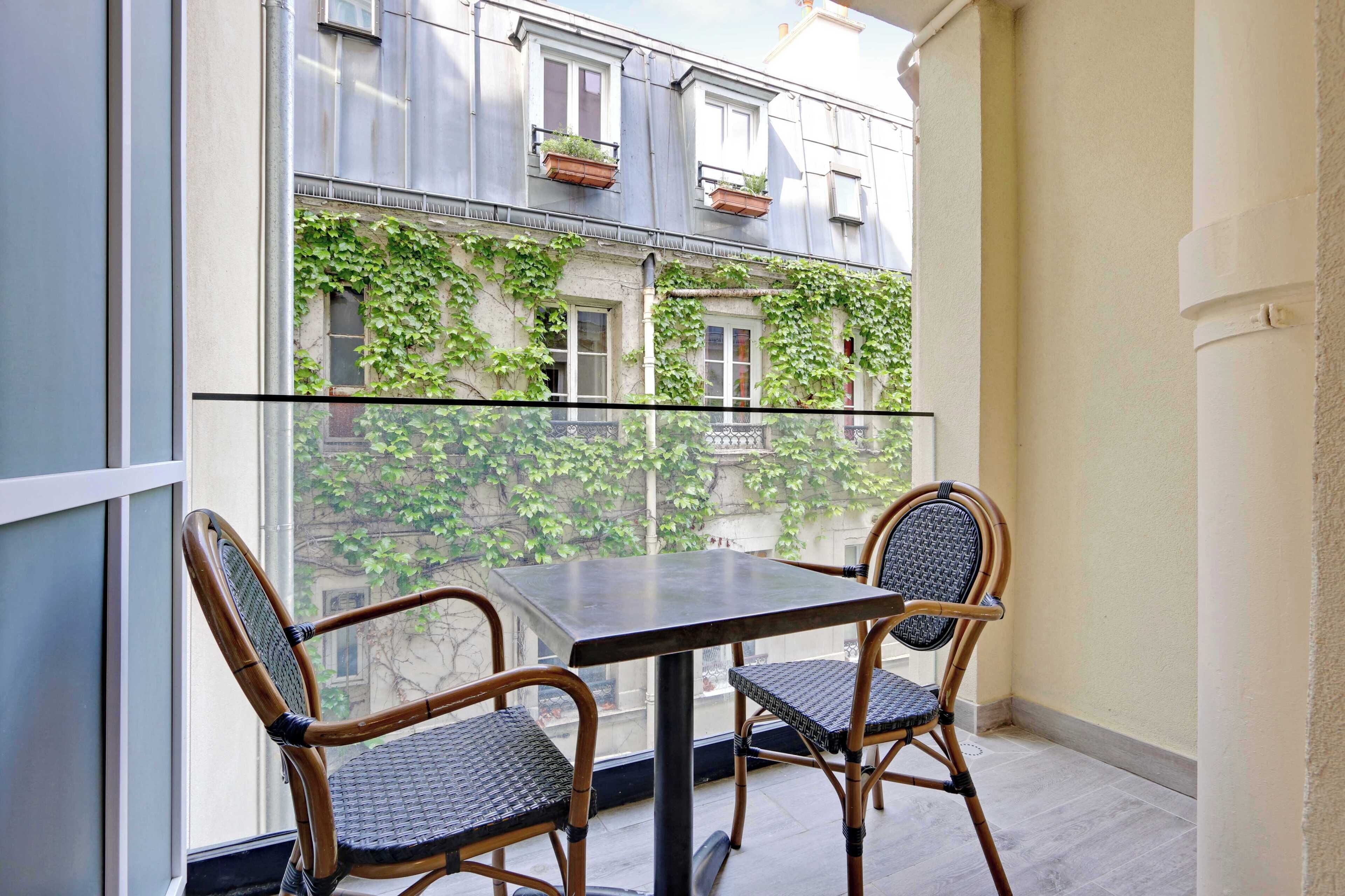 Un balcon doté d’une paroi en verre, de deux fauteuils en osier et d’une table.