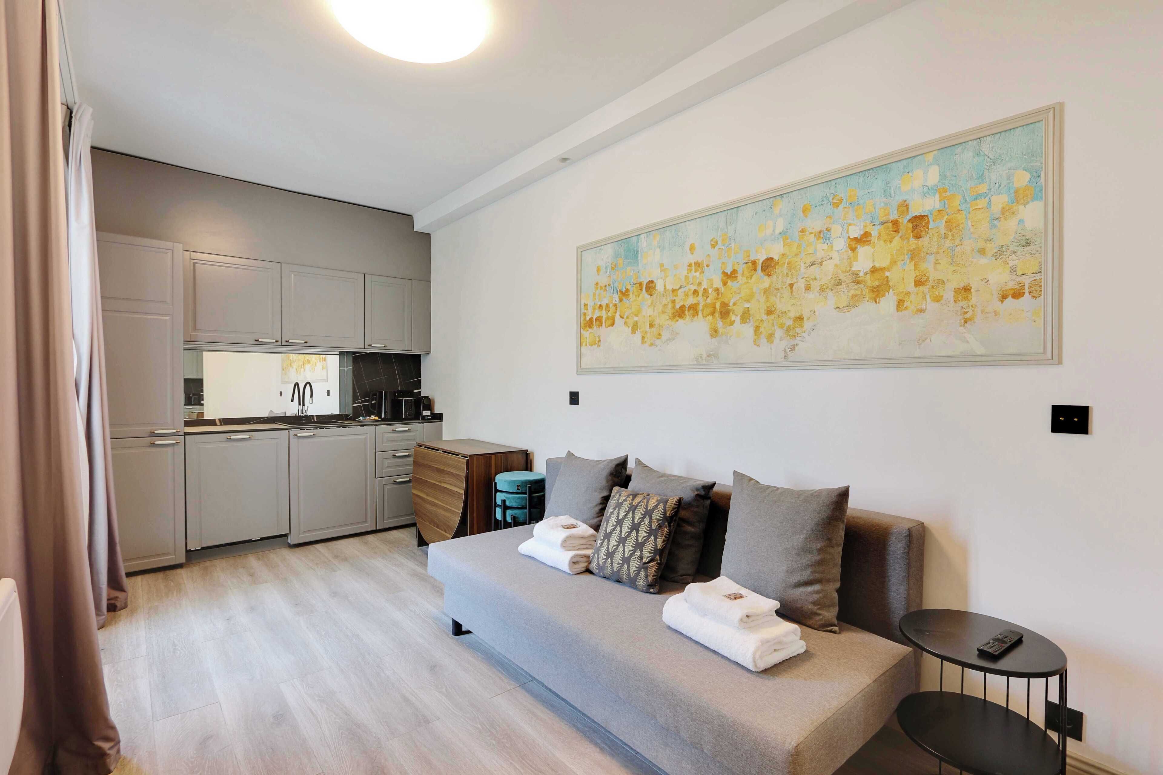 Una sala moderna con un sofá gris, una pequeña mesa redonda y una zona de cocina al fondo.
