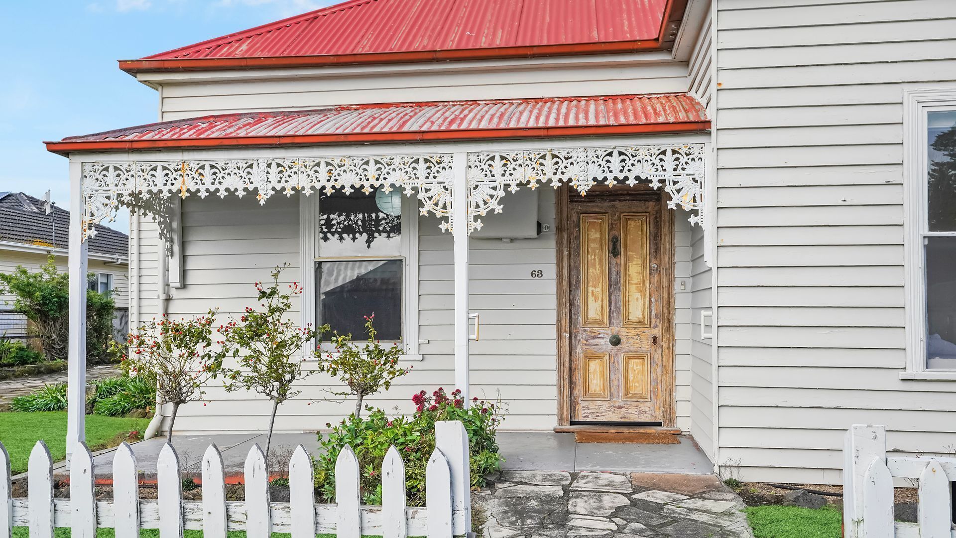 Una casa bianca con tetto rosso, una porta di legno e un portico con decorazioni in pizzo.