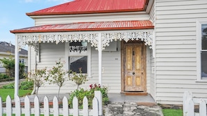 A white house with a red roof, a wooden door, and a porch with lace trim. - Hewlett Cottage - Central Pet Friendly (Port Fairy)