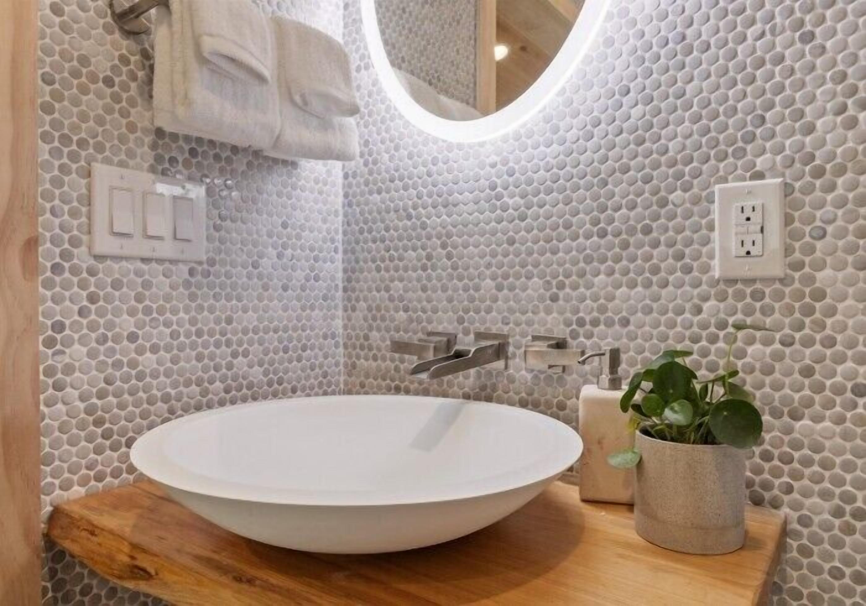 A bathroom with a white sink, a wooden countertop, a potted plant, and a tiled wall with a hexagonal pattern.