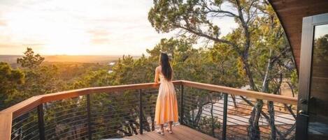 A woman standing on a wooden deck overlooking a hot tub and a scenic landscape.