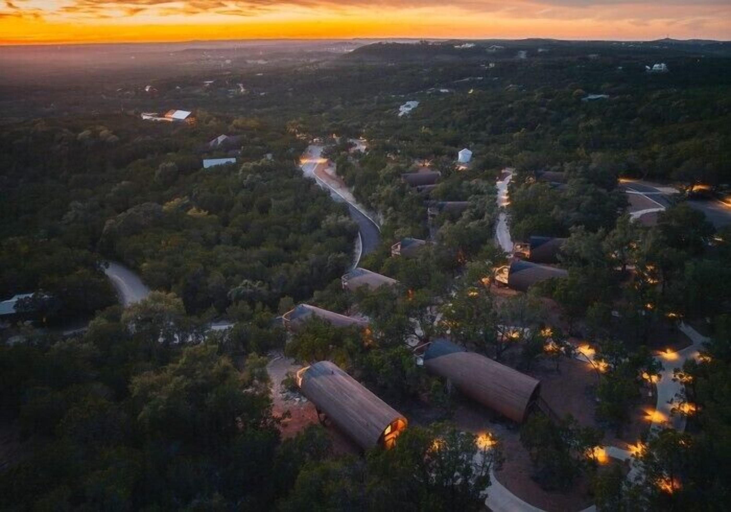 An aerial view of a resort with multiple cabins, winding roads, and surrounding forested areas.