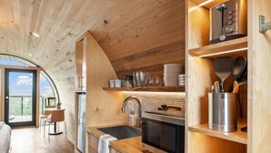 Une cuisine moderne avec des meubles en bois, un four encastré et un évier. On y trouve également un coin repas avec une table et des chaises, ainsi qu’une grande fenêtre offrant une vue sur l’extérieur.