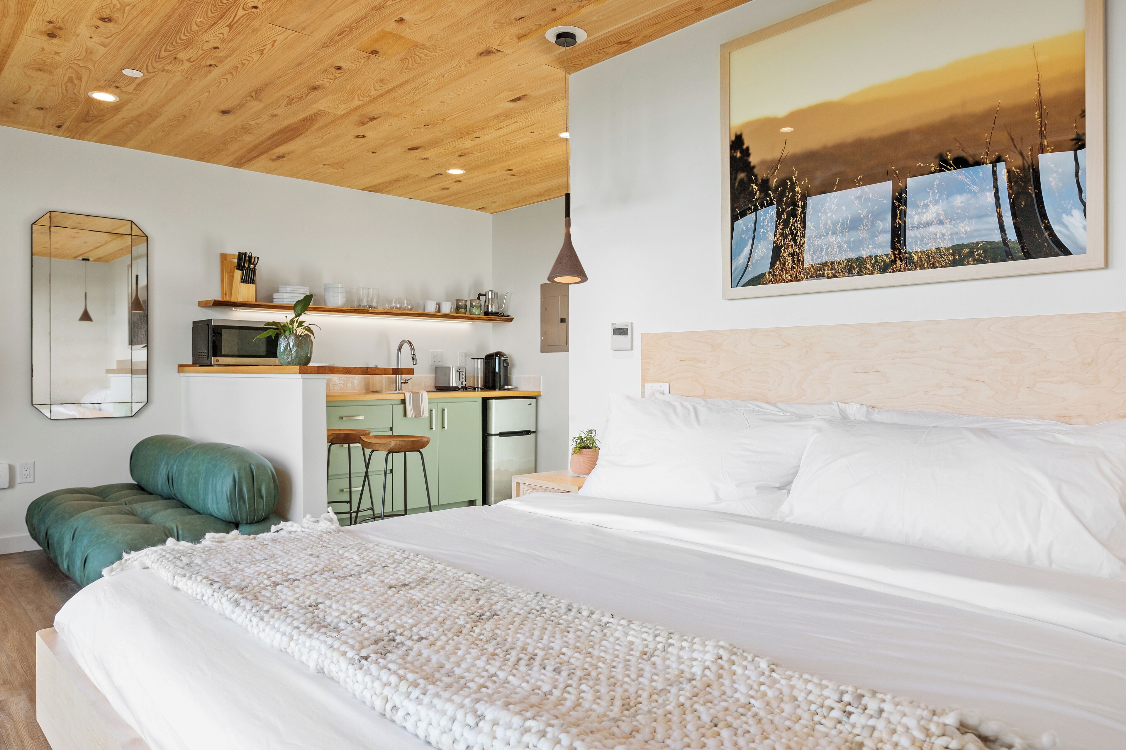 Un dormitorio moderno con una cama grande, techo de madera, zona de cocina y un cuadro grande enmarcado en la pared.