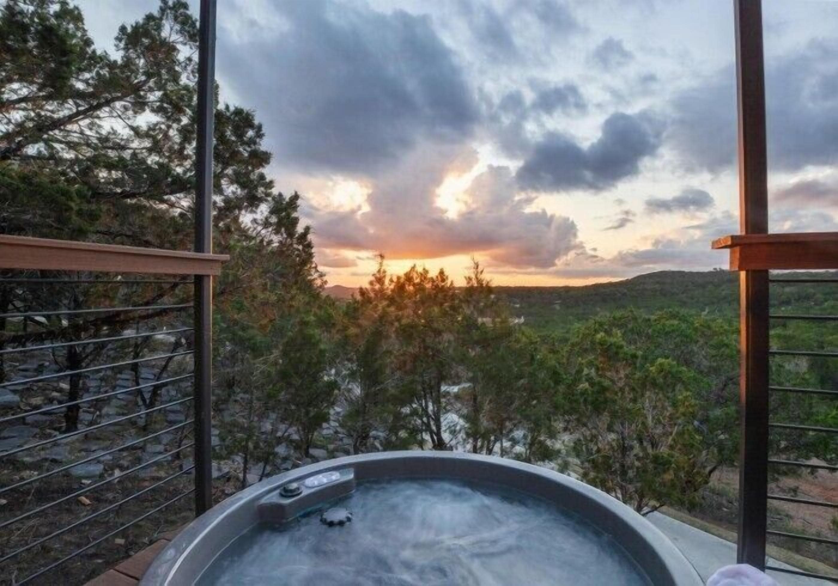 A hot tub with a scenic view of trees and hills during sunset.