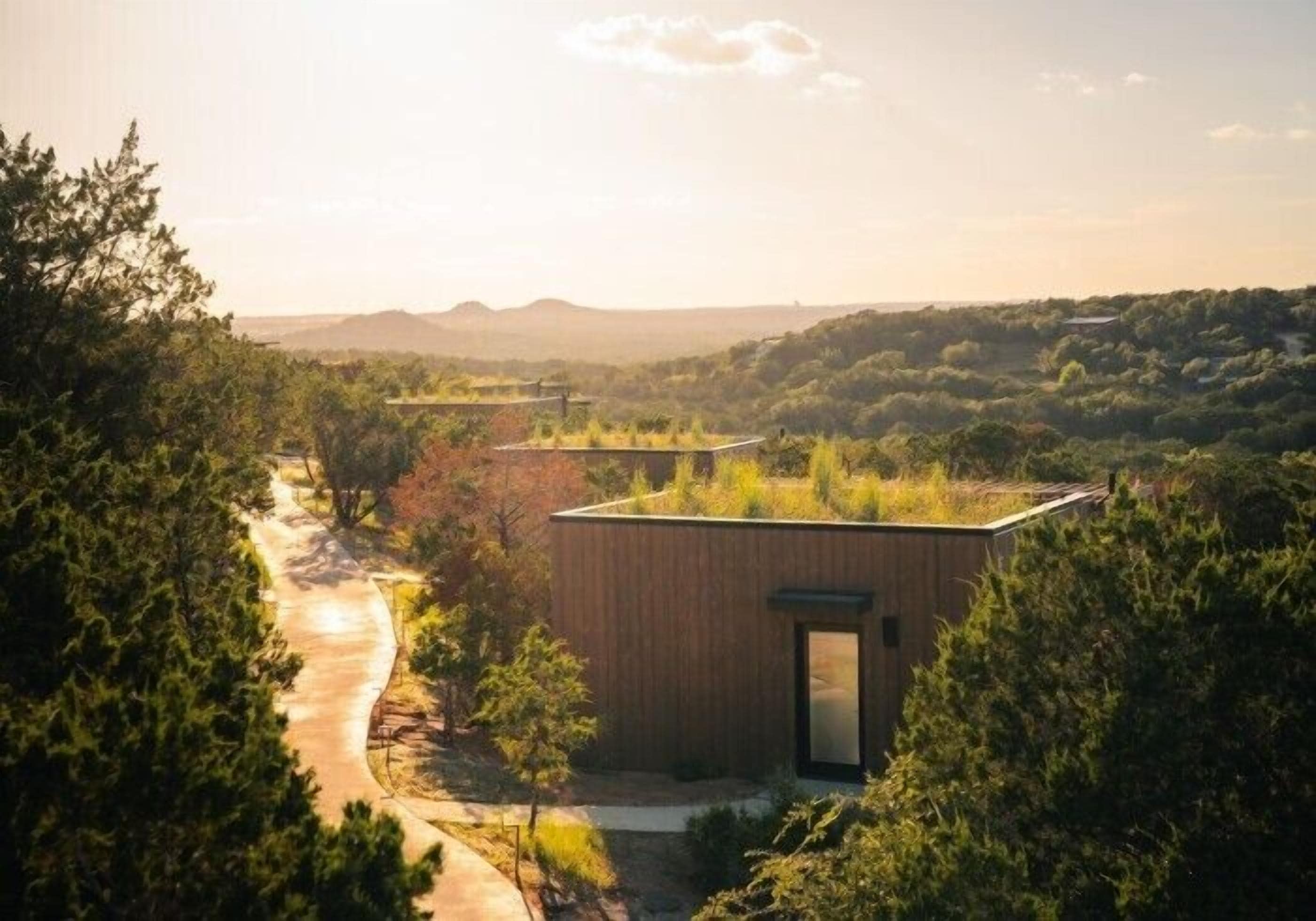 Un edificio moderno de techo plano, rodeado de abundante vegetación y un sendero serpenteante.