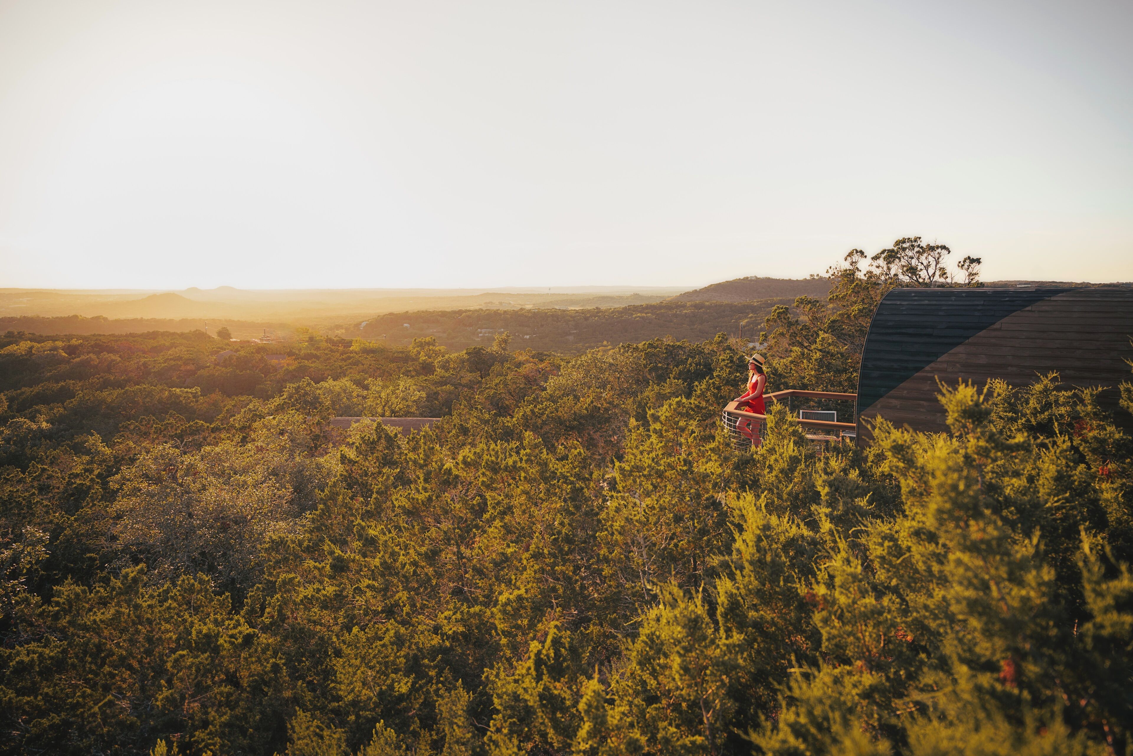 A person standing on a roof overlooking a forested landscape with distant hills.