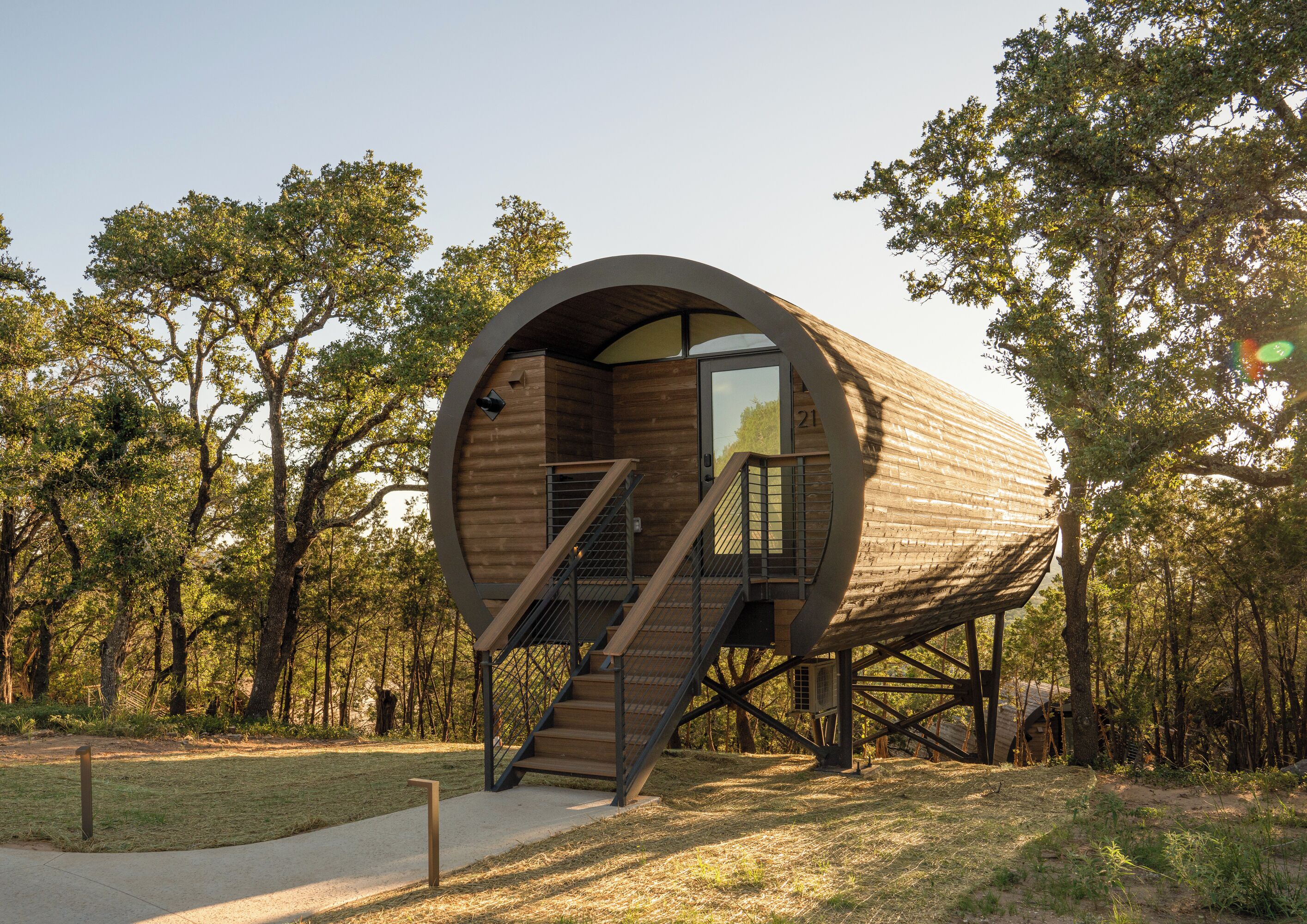 A cylindrical wooden structure with a staircase leading to a door, surrounded by trees.