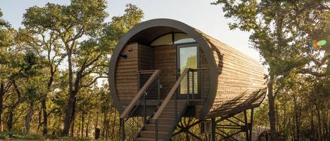 A cylindrical wooden structure with a staircase leading to a door, surrounded by trees.