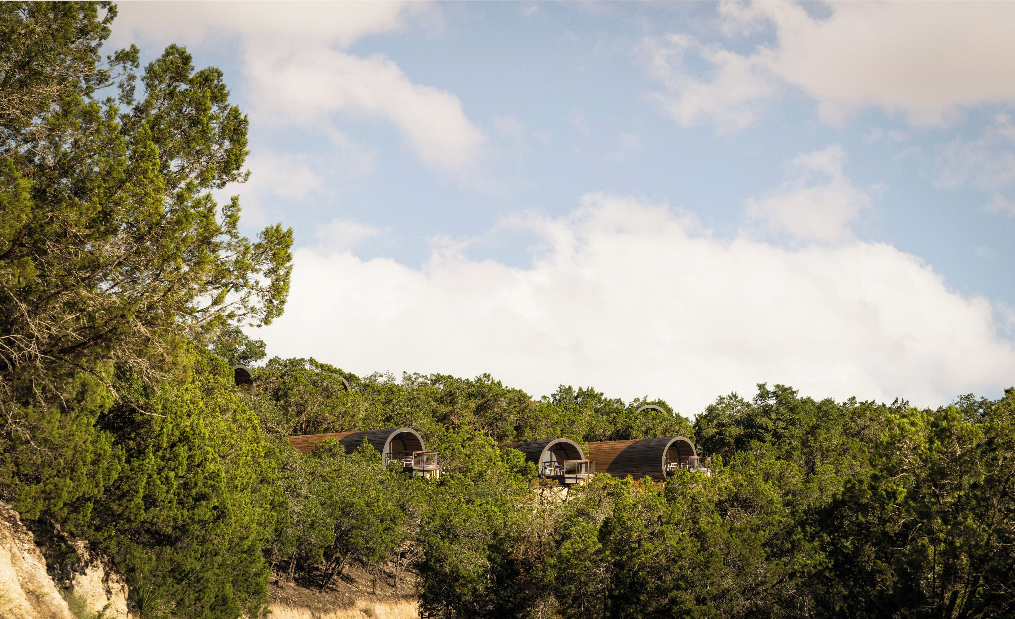 Three arched cabins nestled among dense trees, with a clear sky above.