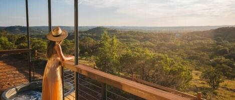 Una persona está de pie sobre una terraza de madera con vistas a un paisaje exuberante.