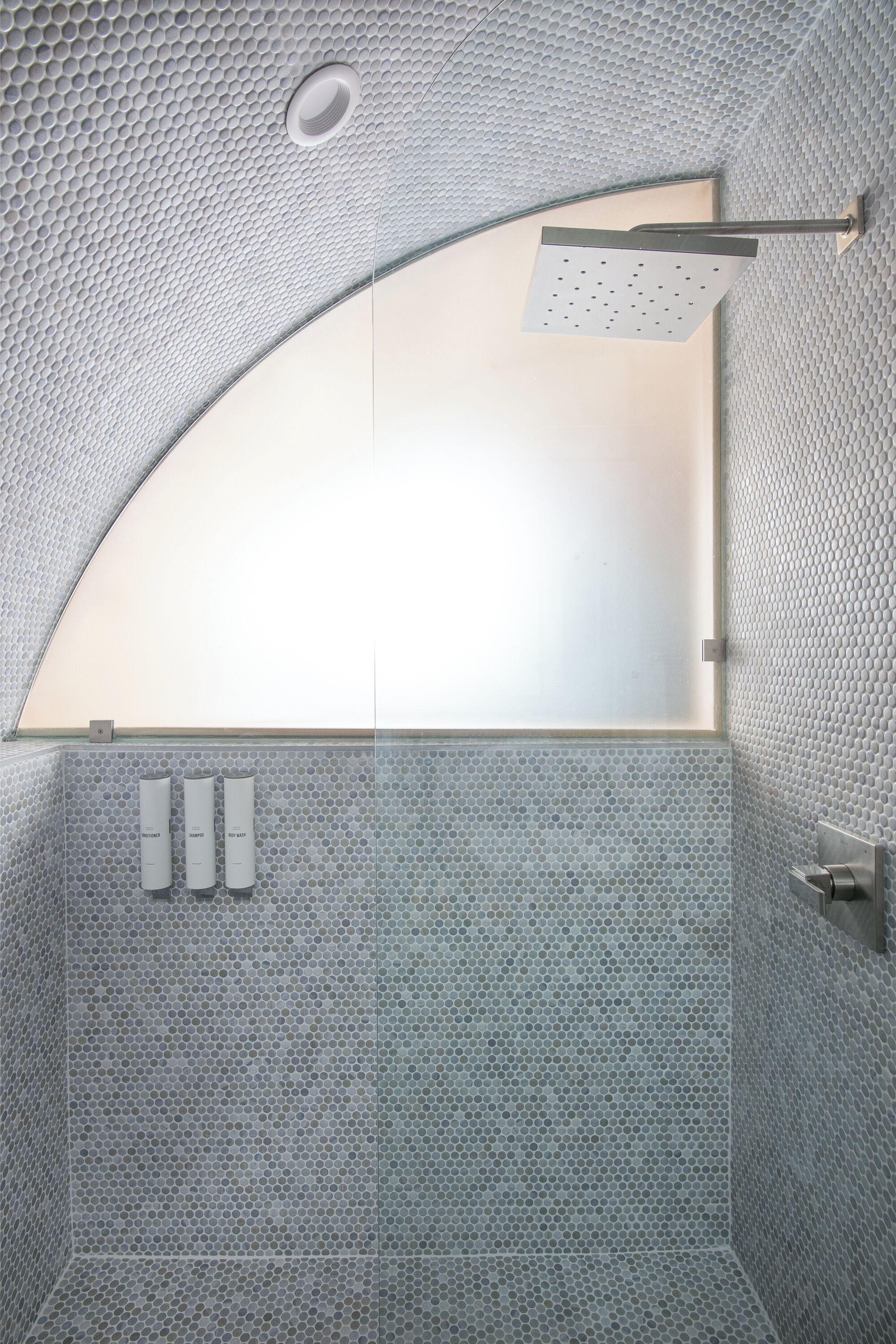 Un baño moderno con techo curvo, ducha y ventana de vidrio esmerilado.