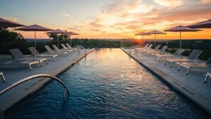 Un espace piscine avec des chaises longues et des parasols, entouré d’une clôture en bois, au coucher du soleil.