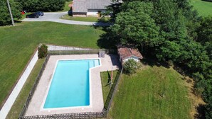 Vista aérea de una propiedad residencial con piscina, rodeada por una valla y abundante vegetación.