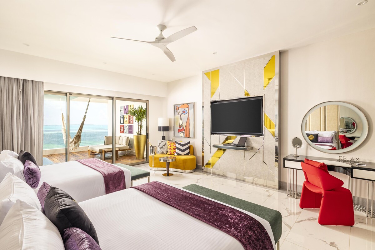 A hotel room with a bed, a desk, a TV, a mirror, and a view of the ocean.