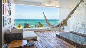 A room with a wooden floor, a hammock, a sofa, a small table, and a large window with a view of the ocean. - Hotel Mousai Cancun Ocean Front Adults Only - All Inclusive (Punta Sam)