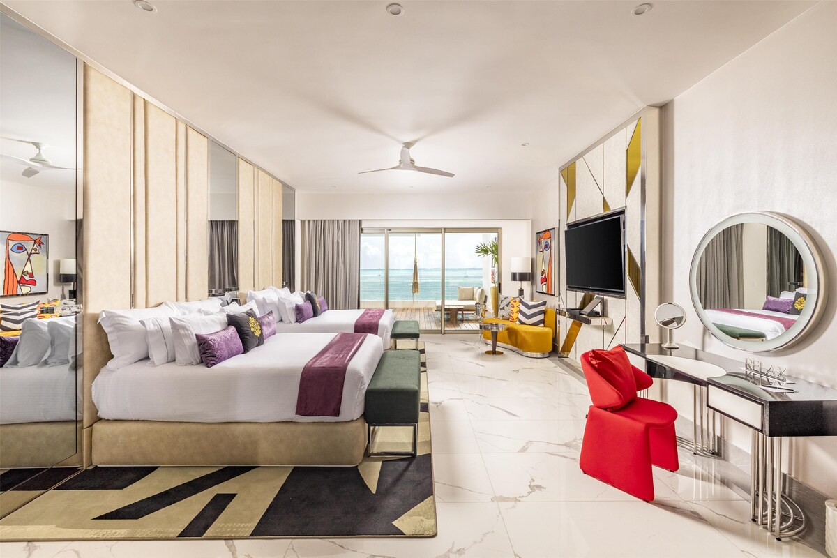 A hotel room with a bed, a desk, a chair, a TV, and a view of the ocean.