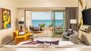 A hotel room with a bed, a sofa, a chair, a TV, and a balcony with a view of the sea. - Hotel Mousai Cancun Ocean Front Adults Only - All Inclusive (Punta Sam)