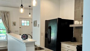 Una cocina moderna con un refrigerador negro, encimeras de granito e iluminación colgante.