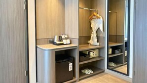 Una habitación de hotel moderna con armario empotrado, un pequeño rincón de descanso con mesa y sillas, y un espejo.
