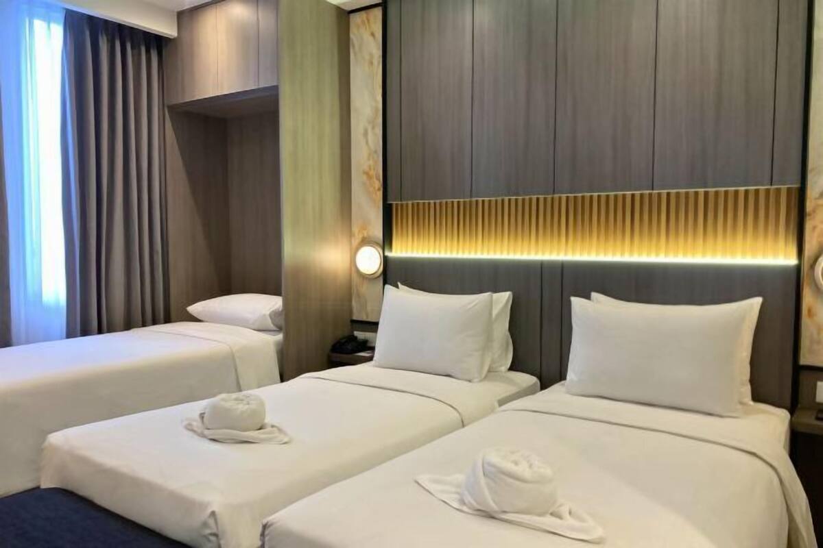Hotellihuone, jossa on kaksi sänkyä, yöpöytä, seinään kiinnitetty valaisin ja ikkuna, jossa on verhot.