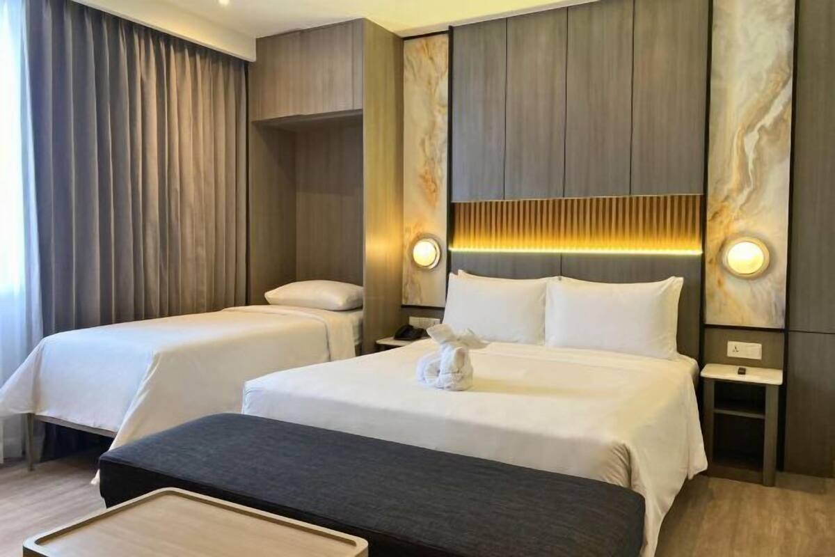 Hotellihuone, jossa on kaksi sänkyä, yöpöytä, lamppu ja seinään kiinnitetty valaisin.