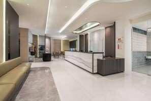 Un moderno vestíbulo de hotel con mostrador de recepción, zona de estar y pared de vidrio.