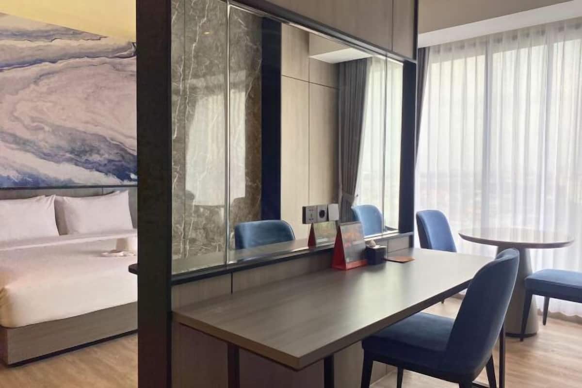 Hotellihuone, jossa on sänky, työpöytä tuoleineen, suuri peili ja ikkunasta avautuva näkymä kaupunkiin.