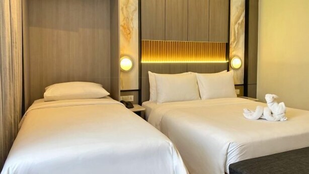 Una habitación de hotel con dos camas, una mesita de noche con lámpara y un aplique de pared.