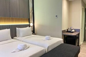 Une chambre d’hôtel avec deux lits, un banc, une petite table avec une bouilloire et un luminaire fixé au mur.