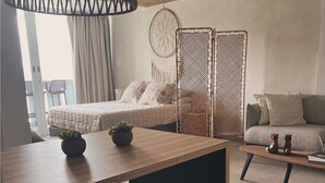 A modern, well-lit room with a wooden dining table, two black stools, a bed with patterned pillows, a grey sofa, and a decorative wall hanging. - Seaside getaway in Isla Verde beach for 4 guest. Book now! (Carolina)