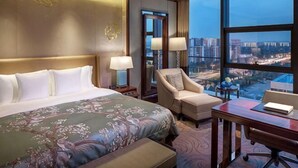 Ein Hotelzimmer mit einem großen Bett, einem Schreibtisch, einem Sessel und Blick auf die Stadt.